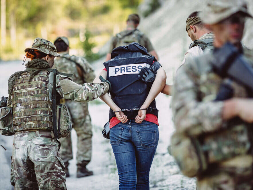 Member of the press in a flak jacket being led away by armed forces