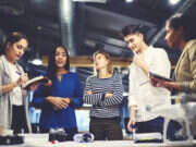 A group of people are gathered around a table taking notes, illustrating a story about an FT Strategies survey on diversity in news organisations.