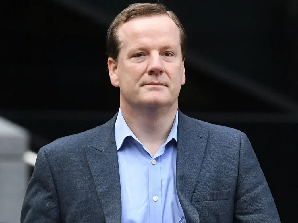 Charlie Elphicke dressed in a suit jacket, blue shirt and jeans and walking with a neutral expression on his face as he looks at the camera