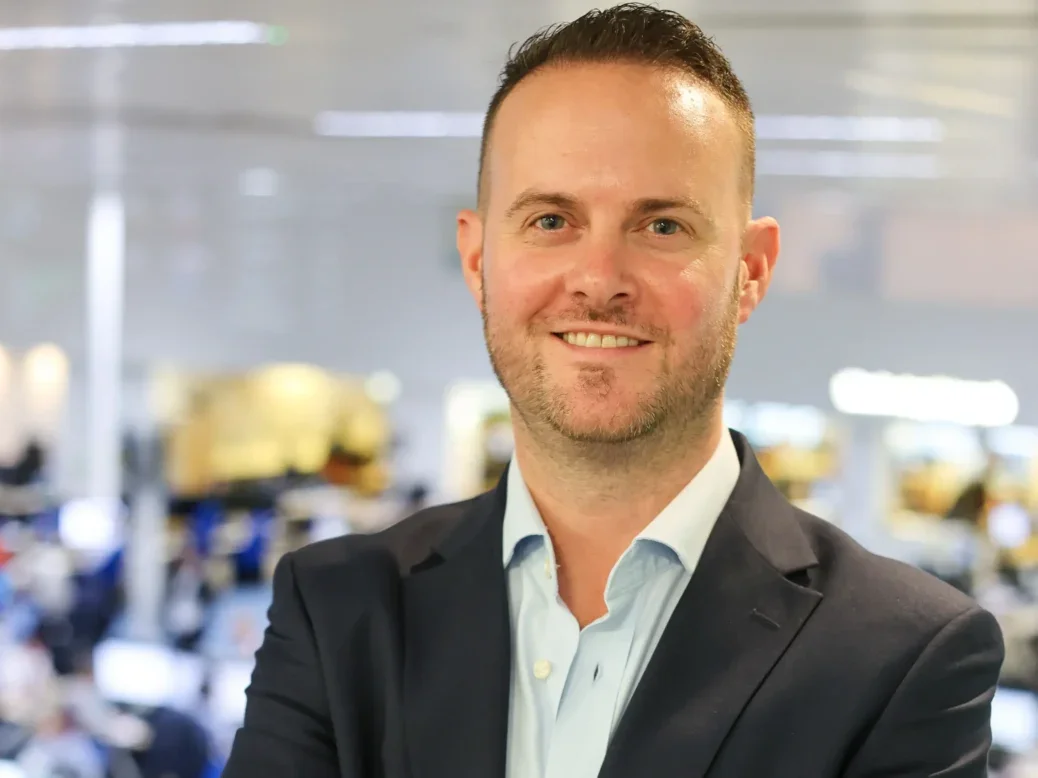 Telegraph director of technology Dylan Jacques standing in front of a newsroom backdrop