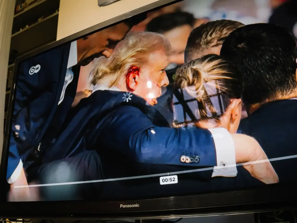 Picture shows TV with paused image of Donald Trump with a bleeding ear being escorted by Secret Service agents around him